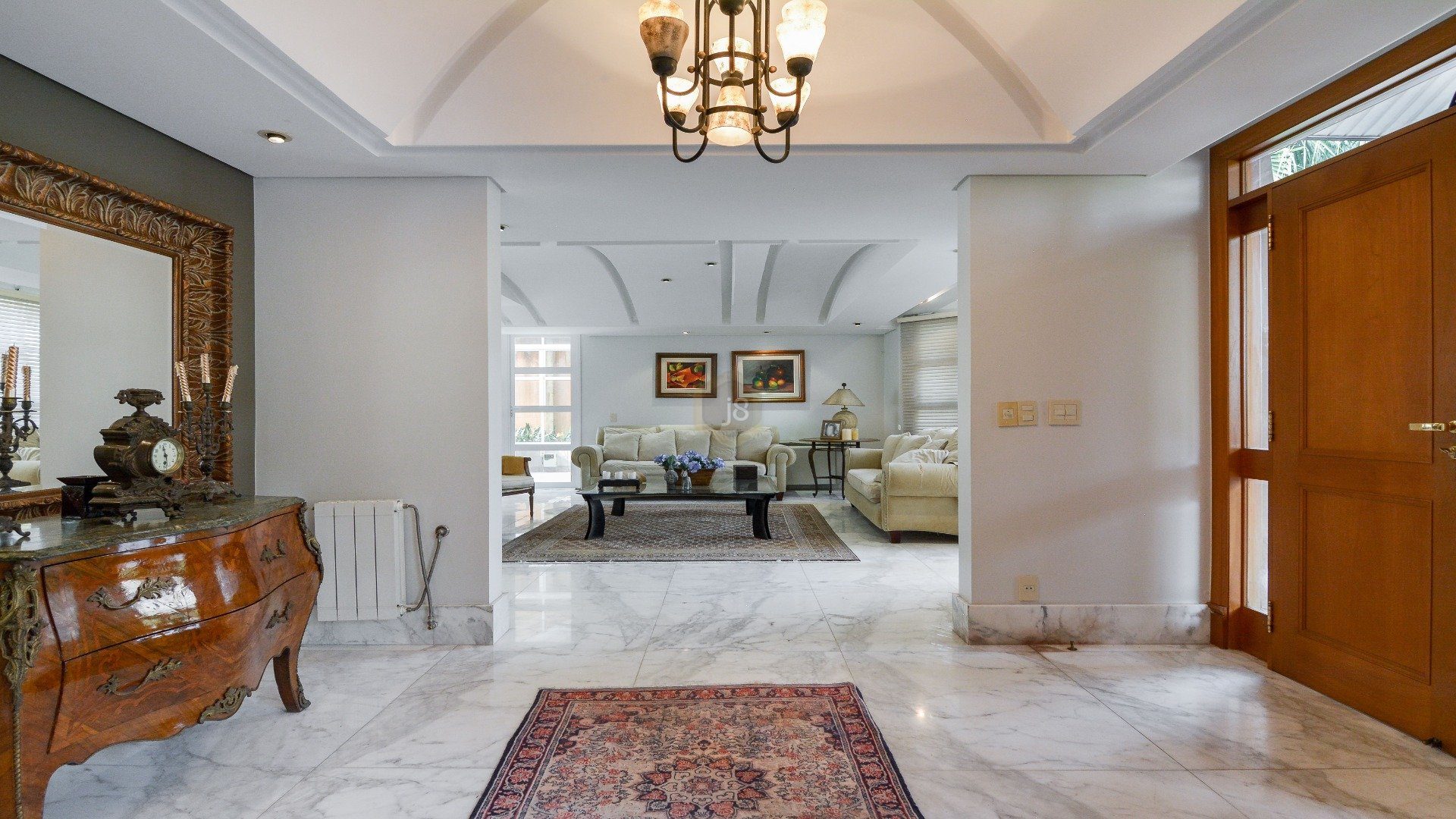 Entrada de casa com espaço formado por tapete e lustre que leva à sala