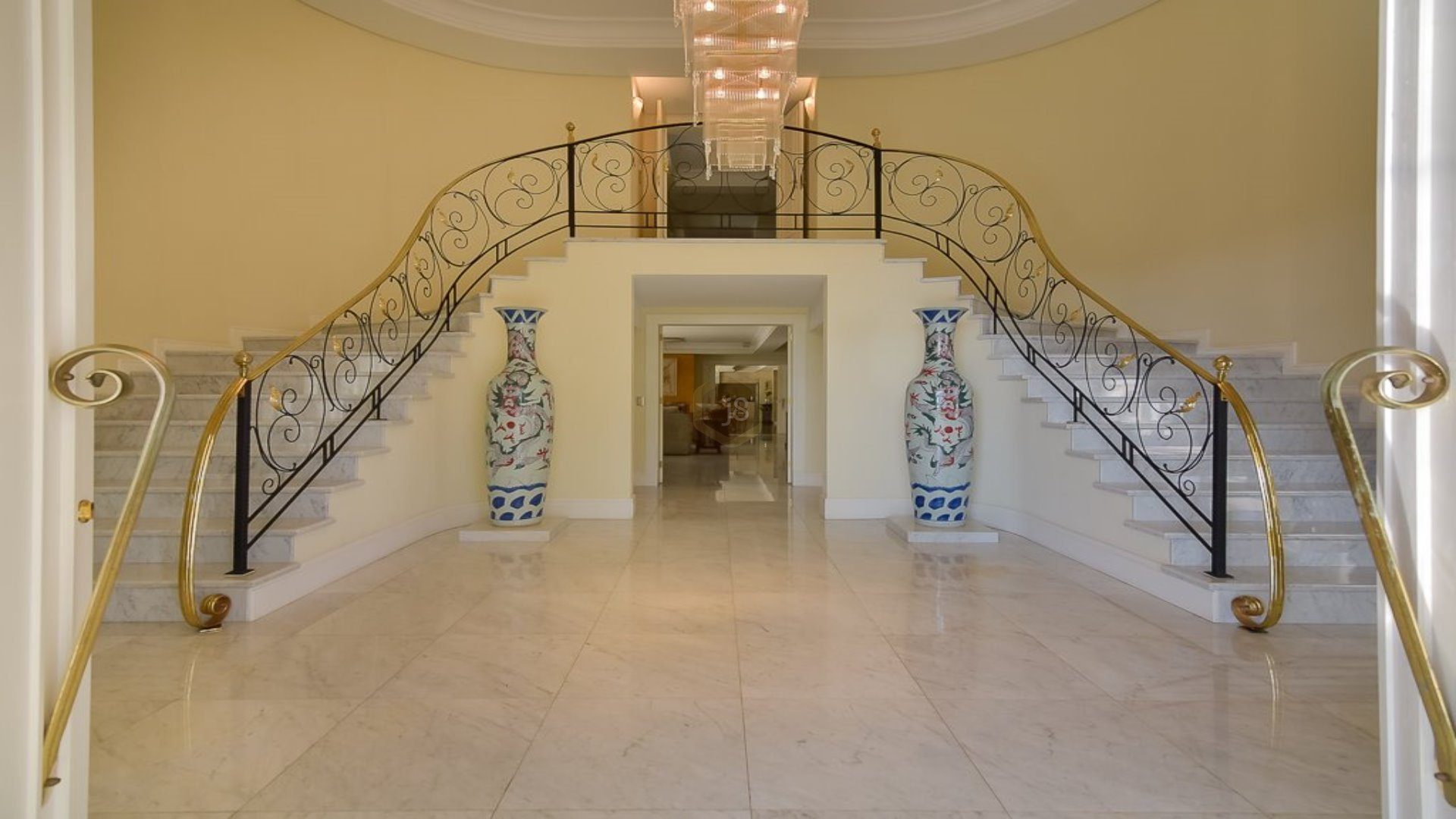 Hall de entrada com pé-direito duplo e escada em metais dourados com lustre e dois grandes vasos